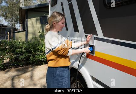 Donna che collega il cavo di alimentazione al camper in campeggio con allacciamento elettrico per viaggiare Foto Stock