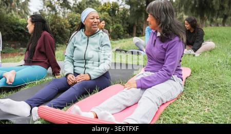 Donne multirazziali che fanno esercizi di yoga all'aperto nel parco cittadino - stile di vita sano e concetto di sport - attenzione principale sul volto di donna anziana africana Foto Stock