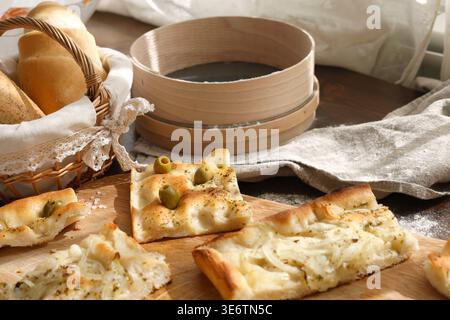 Fette di focaccia italiana artigianale con olive e cipolle su tavola di legno con tradizionale setaccio di farina. Lo scatto ad angolo alto offre una varietà di riprese fatte in casa Foto Stock