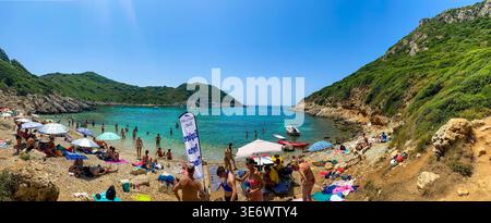 Panorama editoriale della spiaggia di Porto Timoni a Corfù. Affollata baia doppia con acqua turchese e lussureggianti colline verdi. Kerkyra, Grecia, 13 luglio 2023 Foto Stock