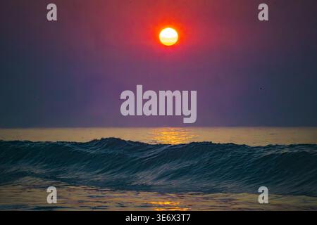 Spettacolare tramonto rosso sull'oceano scuro e sulle montagne Foto Stock