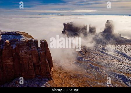 Rocce rosse spolverate di neve che si innalzano sopra il mare di nuvole nella Monument Valley sul confine tra Arizona e Utah, sotto il suggestivo cielo blu. Foto Stock