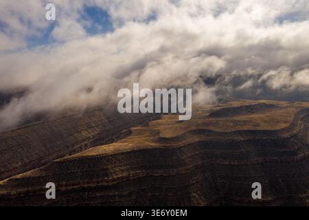 Vista aerea dei suggestivi canyon a strati e delle mesa al Gooseneck State Park, Utah, con nuvole basse e luce dorata sull'aspro paesaggio del deserto. Foto Stock