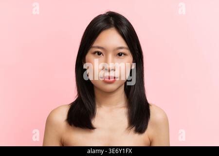 Bella giovane donna con capelli neri dritti si staglia sullo sfondo rosa in Studio Foto Stock