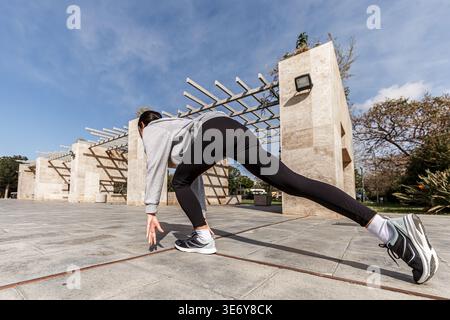 Una giovane donna si sta preparando a correre in un parco all'aperto in Spagna. Sta allungando le gambe e regolando la postura in preparazione all'allenamento Foto Stock