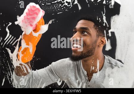 Sapone per la pulizia di lavoratori neri sorridenti sud su una finestra di vetro Foto Stock