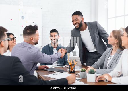 Due uomini d'affari che stringono la mano, seduti alla scrivania Foto Stock