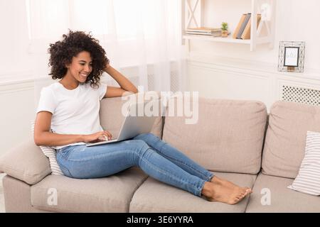 Donna attraente che utilizza un notebook mentre si rilassa sul divano Foto Stock