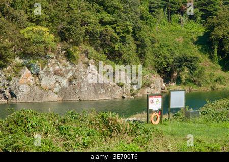 Accanto al fiume Taehwa, vicino alla roccia di Seonbawi a Ulju-gun, è presente un cartello segnaletico, con una scogliera rocciosa, un pennello verde e un'acqua lenta che riempie la cornice. Foto Stock