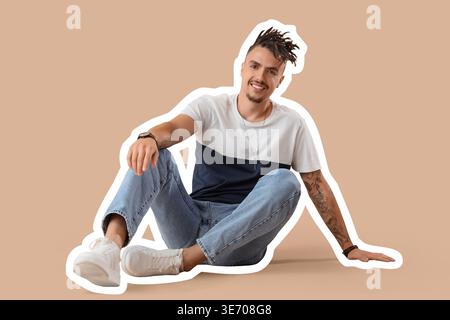 Giovane uomo tatuato con dreadlock seduto su sfondo beige Foto Stock