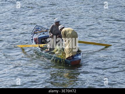 Due uomini in una piccola barca da pesca di legno con pesci catturati nella loro rete dal fiume Nilo Foto Stock