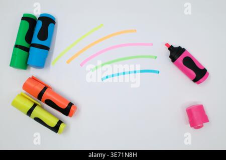 I mini pennarelli dai colori vivaci (verde, blu, arancione, giallo e rosa) sono disposti con i relativi cappucci visibili. I tratti di colore corrispondenti vengono tracciati accanto a eac Foto Stock