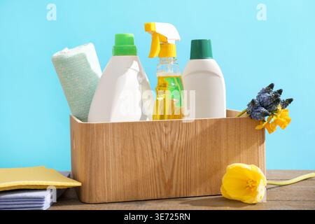 Pulizia di primavera. Detersivi, forniture e fiori su tavola di legno su sfondo azzurro, primo piano Foto Stock