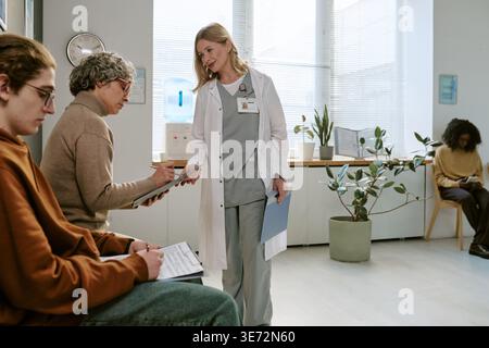 Dottoressa donna che assiste donna anziana con i moduli di assunzione clinica Foto Stock