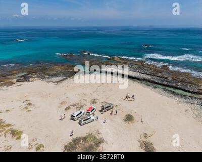 Vista aerea delle auto parcheggiate sulla spiaggia sabbiosa che incontrano l'oceano turchese, un netto contrasto tra terra arida e mare vibrante, Erissel, Socotra, Yemen. Foto Stock