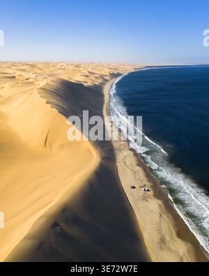 Vista aerea dell'incontro tra il deserto dorato e il mare blu profondo, dove le onde si infrangono sulla spiaggia sabbiosa di Anichab, Erongo, Namibia. Foto Stock