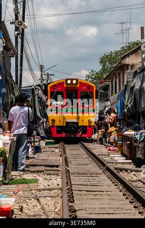 Autentica esperienza del mercato tailandese di strada al mercato ferroviario di Maeklong con venditori di pesce, bancarelle di prodotti e un treno che attraversa il centro Foto Stock