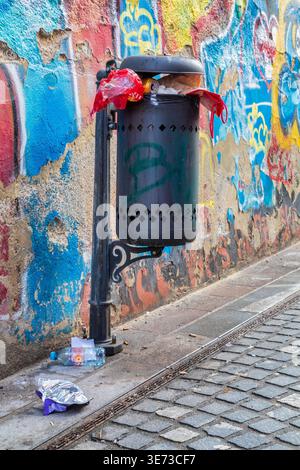 Traboccante di rifiuti pubblici con rifiuti per la strada di fronte a un muro coperto di graffiti sul cesta Trubarjeva a Lubiana, Slovenia Foto Stock