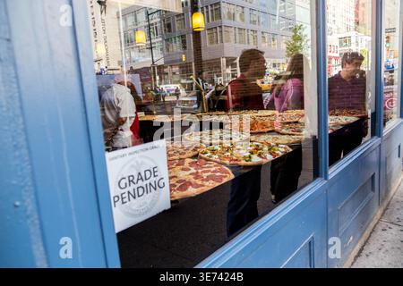 Varietà di pizze intere esposte in una vetrina della pizzeria di New York City accanto a un cartello di ispezione sanitaria "Grade Pending" Foto Stock
