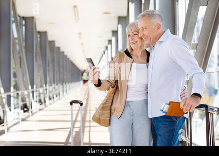 Coppia matura appoggiata alla ringhiera dell'aeroporto che guarda lo smartphone insieme Foto Stock