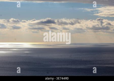 Le spettacolari nuvole si dividono mentre i raggi del sole illuminano un mare scintillante con delicate tonalità dorate. Foto Stock