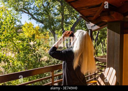 Donna bionda anziana che usa binocoli sul portico in autunno Foto Stock