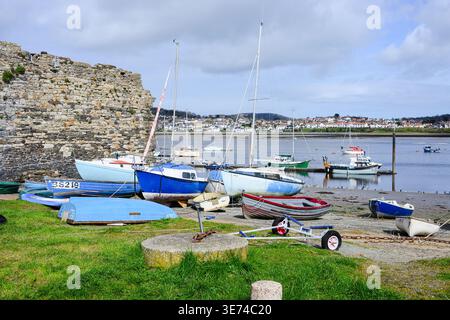 Conwy, Galles, Regno Unito - 26 marzo 2026; piccole imbarcazioni lungo l'estuario del fiume Conwy e parete di pietra sulla spiaggia Foto Stock
