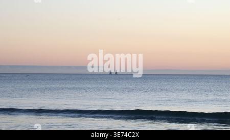 Vista sulla spiaggia di due barche a vela in lontananza al tramonto sull'isola di Mauritius. Foto Stock
