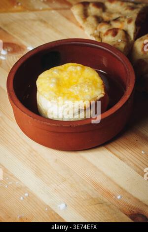 Formaggio Camembert al forno con crosta fusa in una tradizionale pentola di argilla servita con focaccia su un tavolo di legno. Foto Stock