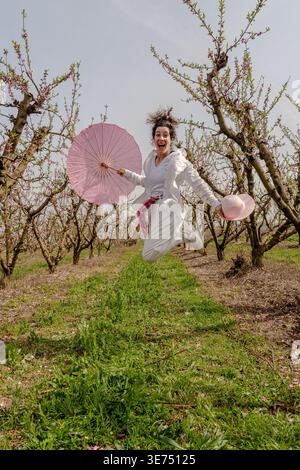 Donna eccitata che salta con l'ombrello nel frutteto primaverile Foto Stock