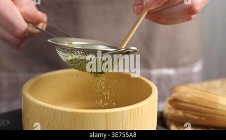 Donna setacciando polvere di matcha in ciotola, primo piano Foto Stock