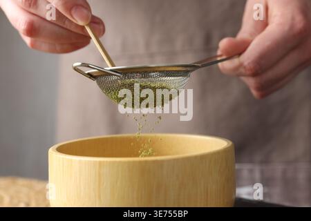 Donna setacciando polvere di matcha in ciotola, primo piano Foto Stock