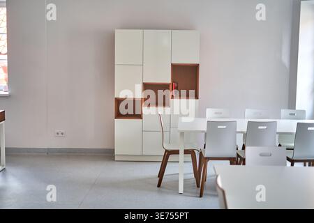 Spazio interno minimalista moderno con un tavolo da pranzo bianco e sedie bianche coordinate con gambe in legno posizionate in primo piano. Dietro il Foto Stock