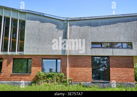 Facciata curva di un edificio modernista con struttura a due piani in materiali contrastanti. Il piano superiore mostra intonaco o stucco grigio Foto Stock
