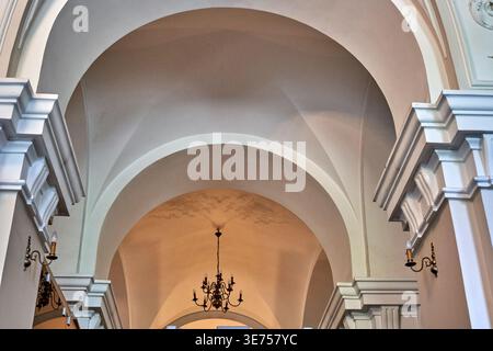 Vista architettonica interna di un edificio storico con un elegante design classico caratterizzato da più archi a volta bianchi e decorazioni ornate Foto Stock