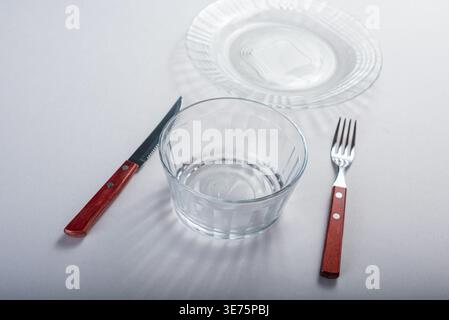 Impostazione del recipiente di vetro pulito con un coltello e una forchetta su una superficie bianca. Le piastre e gli utensili mostrano precisione in un'impostazione minimalista. Pulito, luminoso e prec Foto Stock