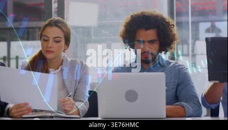 Analista di digitazione maschile che indossa una camicia blu in denim in ufficio, rivedendo documenti con laptop e grafici Foto Stock