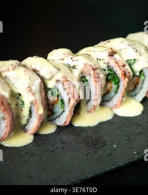 Ricca salsa cremosa condita con sushi roll. Verdure fresche e carne tenera scorrono nel riso. La piastra scura in ardesia aggiunge un contrasto elegante. Perfetto per l'upsca Foto Stock