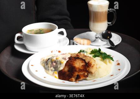 Pasto accogliente servito su vassoio scuro Il recipiente bianco contiene la zuppa montata a vapore. Il piatto caramellato si trova accanto alla crema di patate. Erbe verdi guarnire il piatto con Foto Stock