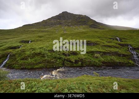 Lussureggiante vegetazione con piccole cascate e una montagna sullo sfondo sotto un soffitto nuvoloso, Glen Etive, Scozia, Regno Unito, Gran Bretagna Foto Stock
