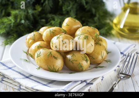 Patate nuove o giovani bollite con burro, Dill fresco e cipolle in un piatto bianco Foto Stock