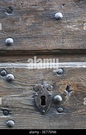 Primo piano di un antico buco della serratura collocato in una porta di legno intemprata con borchie di ferro, che mostra l'età e l'artigianato, evocando mistero, protezione e il passo Foto Stock