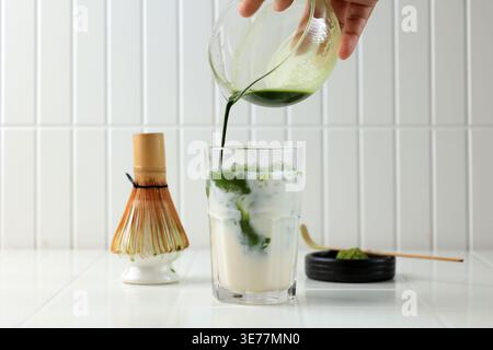 Iced Matcha latte, autentico Matcha latte giapponese preparato con tè Uji. Mano femminile che versa Matcha al latte Foto Stock