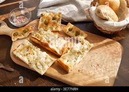Tradizionale assortimento di focaccia italiana con olive verdi e cipolle su tavola rustica di legno. Lo scatto ad angolo alto è dotato di fette di pane fatte in casa con Foto Stock