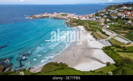 Splendida vista aerea di Caión, Spagna. Questo scatto cattura la spiaggia di sabbia bianca, le onde dell'Atlantico, il villaggio di pescatori sulla penisola e la lussureggiante avidità Foto Stock