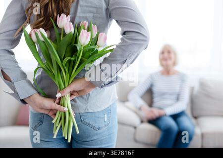 Giovane donna che tiene fiori dietro le spalle per sua madre Foto Stock