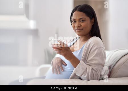 Incinta, tè e ritratto di donna nera sul divano per la salute della maternità, calma e benessere al mattino. Gravidanza, spazio e persona con bevanda calda o. Foto Stock