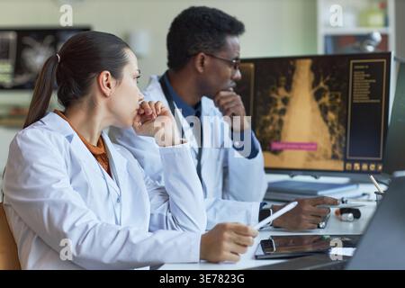 Medio colpo di donna asiatica e uomo afroamericano medici che esaminano la scansione medica sul monitor, consulenza sulla diagnosi e la pianificazione del trattamento. Ideale per il marketing del lavoro di squadra nel settore sanitario Foto Stock