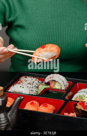 Ragazza in maglione verde che tiene il nigiri dalla scatola bento con le bacchette Foto Stock