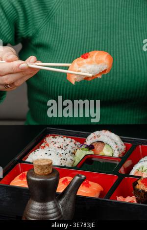 Ragazza in maglione verde che tiene il nigiri dalla scatola bento con le bacchette Foto Stock